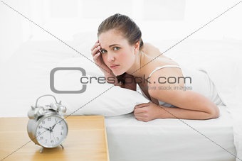 Displeased woman in bed with alarm clock in foreground