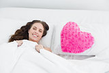 Smiling woman lying in bed with heart  shaped pillow cover