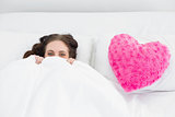Smiling woman lying in bed with heart  shaped pillow cover