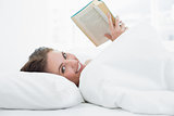 Smiling young woman reading a book in bed