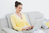 Smiling casual woman using laptop on sofa