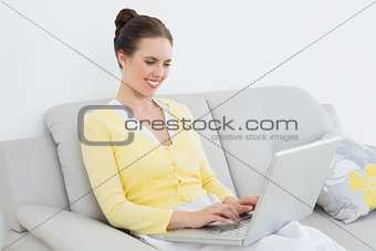 Smiling casual woman using laptop on sofa