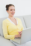 Cheerful casual woman using laptop on sofa