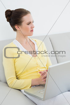 Thoughtful casual woman with laptop sitting on sofa