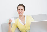 Smiling woman with coffee cup and laptop sitting at home