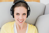 Smiling woman listening music through headphones on sofa