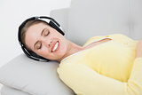 Woman listening music through headphones on sofa