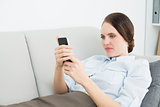 Smartly dressed woman reading text message while lying on sofa