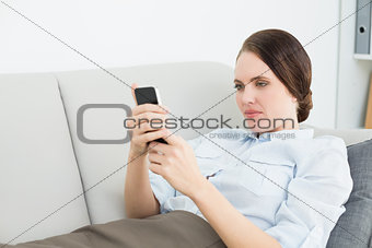 Smartly dressed woman reading text message while lying on sofa