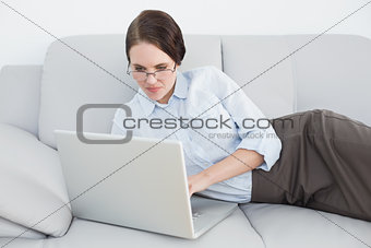 Smartly dressed woman using laptop on sofa