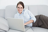 Smartly dressed smiling woman with laptop on sofa