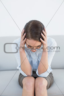 Worried well dressed woman with head in hands on sofa