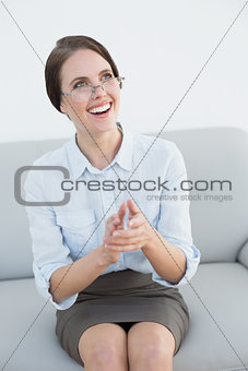 Smiling well dressed woman clapping hands on sofa
