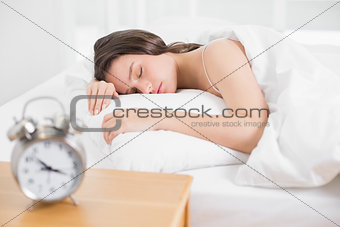 Woman sleeping in bed with alarm clock in foreground