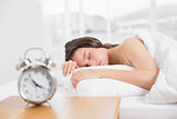Woman sleeping in bed with alarm clock in foreground