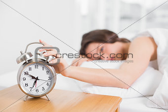 Blurred woman in bed extending hand to alarm clock