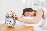 Sleepy blurred woman in bed extending hand to alarm clock