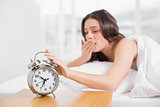 Woman yawning while extending hand to alarm clock