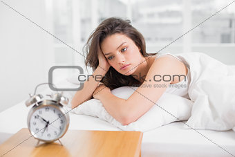 Sleepy woman looking at alarm clock on bedside table