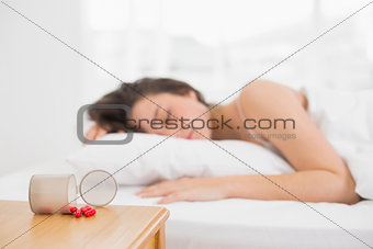 Blurred woman sleeping in bed with pills in foreground