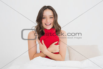 Smiling woman with a hot water bottle in bed