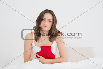 Sad woman sitting with a hot water bottle in bed