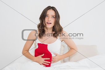 Woman with hot water rubber bag on stomach in bed