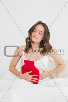 Woman with hot water bottle on stomach in bed