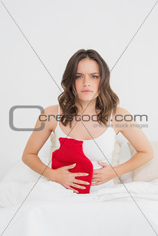 Upset woman sitting with a hot water bottle in bed