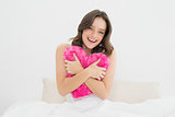 Happy woman hugging heart shaped pillow in bed
