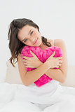 Cute woman hugging heart shaped pillow in bed