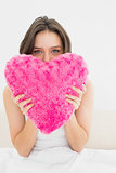 Woman holding heart shaped pillow in bed