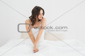 Content woman sitting and looking away in bed
