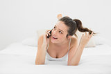 Cheerful casual woman using mobile phone in bed