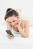 Happy casual woman looking at mobile phone in bed