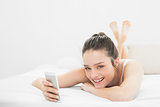 Happy casual woman with mobile phone in bed