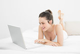 Cheerful woman using laptop in bed