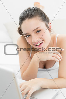 Smiling casual woman using laptop in bed