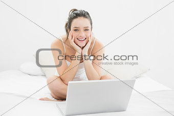 Smiling casual woman with laptop sitting on bed
