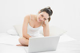 Smiling casual woman with laptop sitting on bed