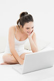 Smiling casual woman with laptop on bed