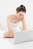 Smiling casual woman using laptop in bed