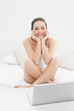 Cheerful casual woman with laptop sitting on bed