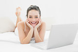 Smiling casual woman with laptop in bed