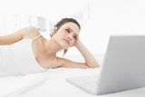 Casual woman looking away by laptop in bed
