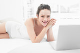 Smiling casual woman with laptop in bed