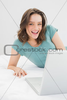 Cheerful casual woman with laptop in bed