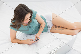 Casual woman text messaging by laptop in bed