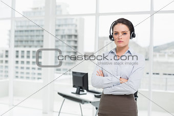 Elegant businesswoman wearing headset with arms crossed in office