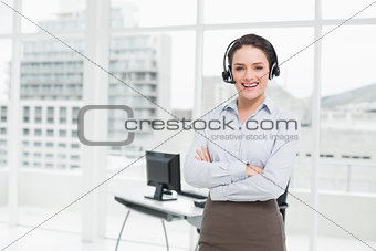 Smiling elegant businesswoman wearing headset with arms crossed in office